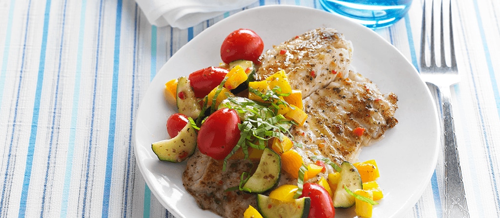 Tilapia fish filets with yellow pepper, zucchini, grape tomatoes and fresh basil covered in Italian Vinaigrette dressing on a plate.  Recipe calls for 7 ingredients, 25 minutes cooking time, 25 minutes prep time, and 4 servings.