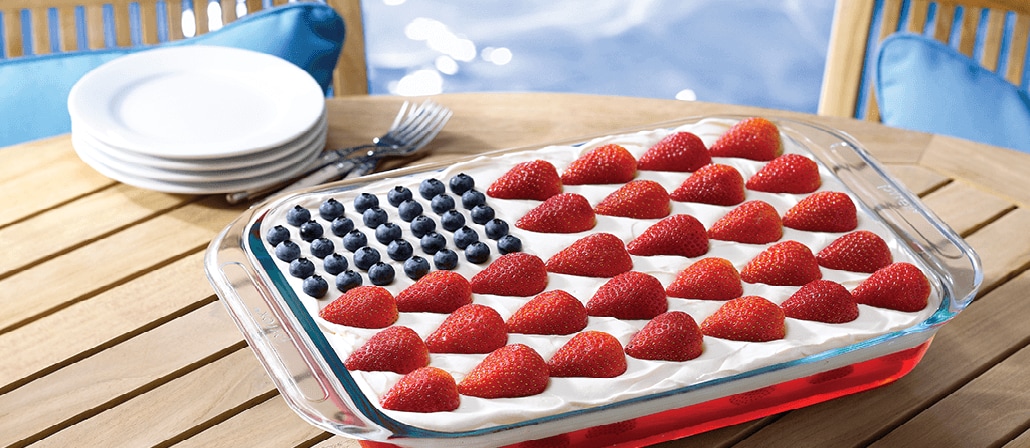 A glass dish with Blueberries and raspberries in a bed of whipped cream cheesecake arranged like the American flag where the blueberries are the stars and the raspberries are the stripes.  Recipe calls for 10 ingredients, 255 cooking time, 20 minutes prep time, and 20 servings.