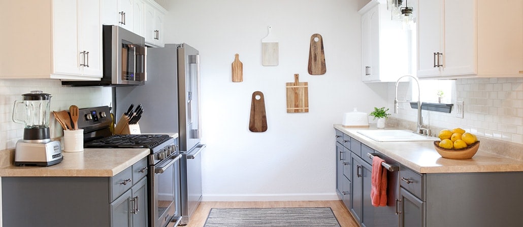 Kitchen with white and gray cabinets, natural wood countertops, stainless steel appliances, and a bunch of wooden cutting boards hanging on the wall.