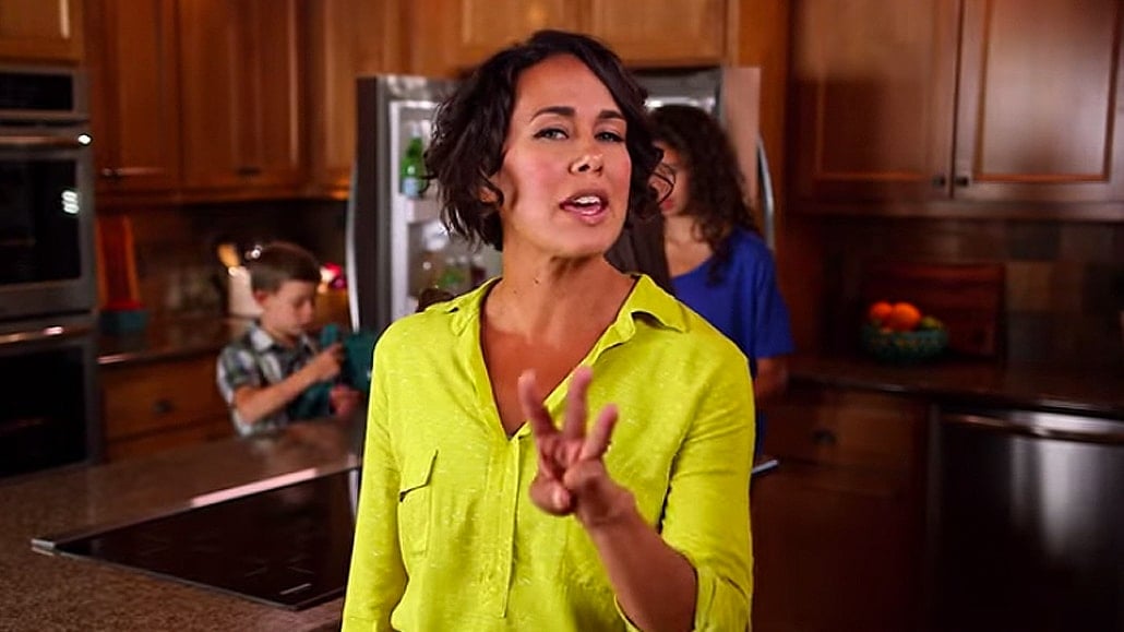 A woman in a yellow shirt standing in a kitchen holding up 3 fingers to details the 3 secrets of a time saving kitchen.
