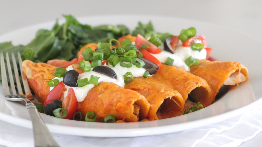A plate of corn tortilla enchiladas with shredded chicken, shredded cheddar cheese, cilantro, covered in sour cream. Recipe calls for 8 servings.