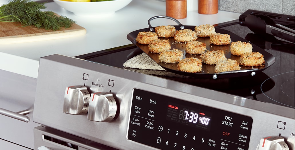 Fried crab cakes in a serving dish sitting on the stovetop of an air-fry-oven.
