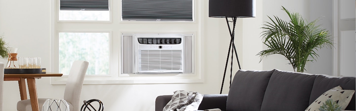 A White window-mounted air conditioner in the window of the living room inside a home.