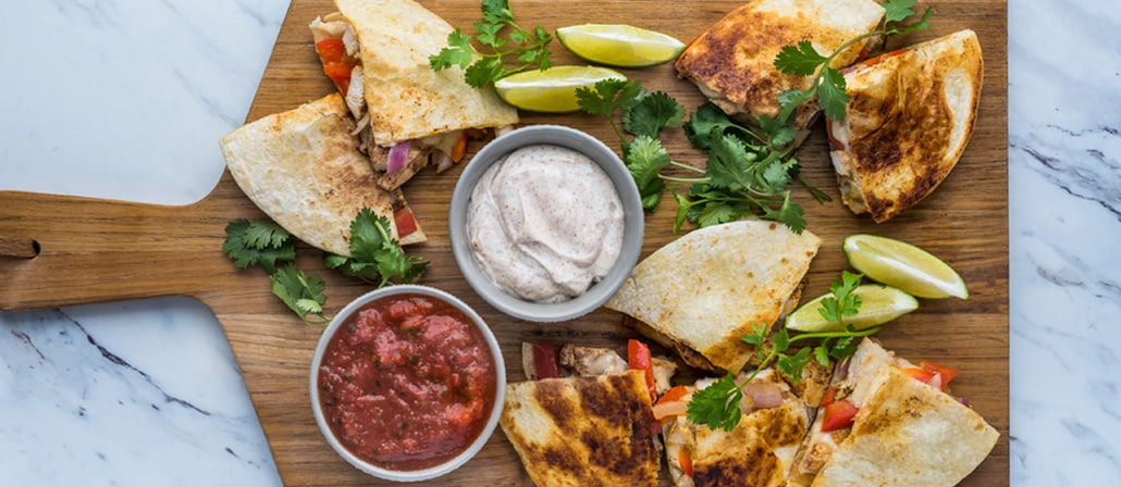Crunchy chicken quesadillas with lime-spiked mayo and spicy salsa on a cutting board.  Recipe calls for 22 ingredients, 45 minutes cooking time, and 6 servings.