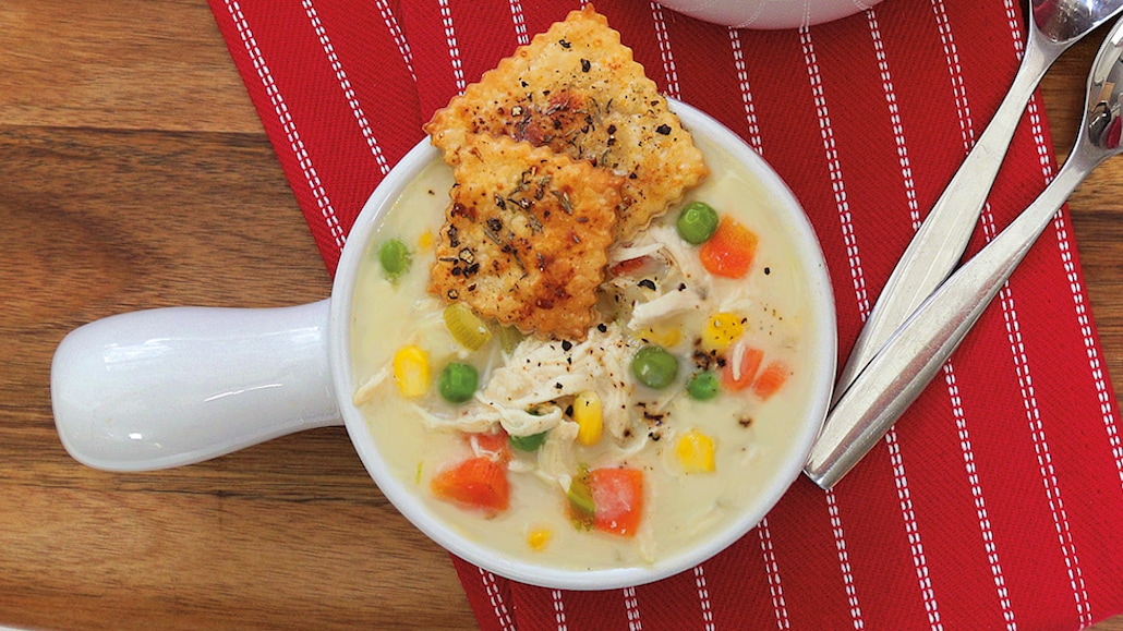Creamy chicken pot pie soup in a bowl with pie crust crackers, onion, celery, carrots and garlic.  Recipe calls for 17 ingredients, 55 minutes cooking time, 35 minutes prep time, and 6 servings.