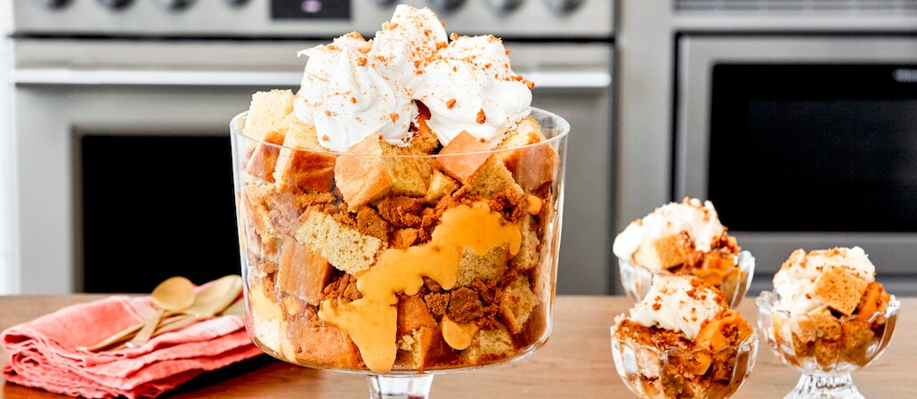 A Glass filled with Pumpkin Spice Trifle topped with whipped cream.  Recipe calls for 17 ingredients, 75 minutes cooking time, 25 minutes prep time, and 15 servings.