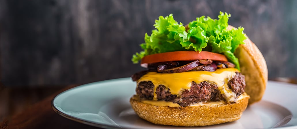 Juicy ¾ pound chuck burger with red onion, lettuce, tomato, and melted American cheese on a burger bun.  Recipe calls for 14 ingredients, 60 minutes cooking time, 10 minutes prep time, and 4 servings.